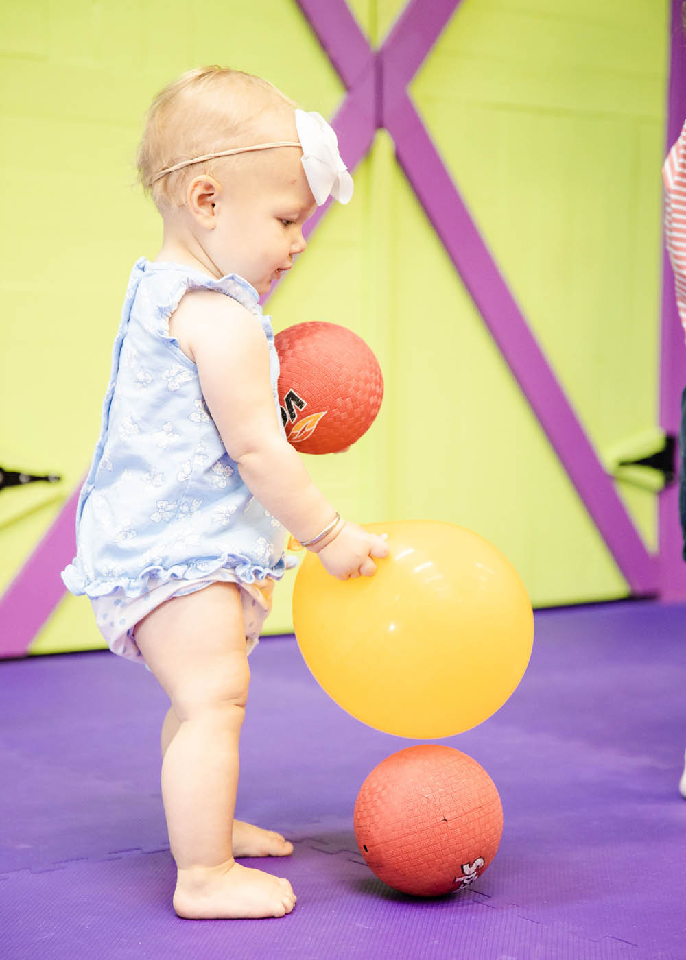 A very little child playing with balls and kid safe equipment in a sports class for 2 year olds with Romp n' Roll.