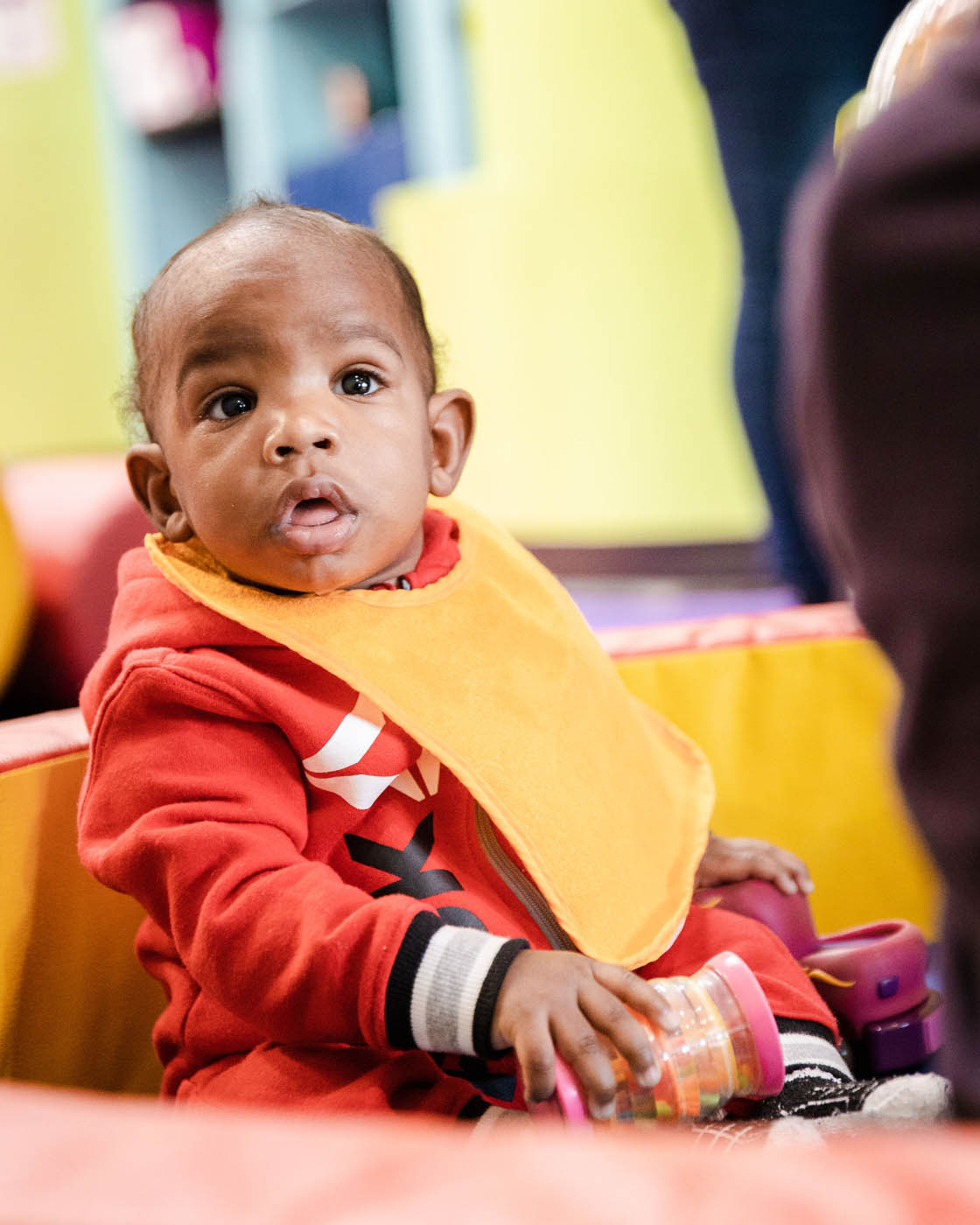 A baby with a yellow bib at a Romp n' Roll facility.