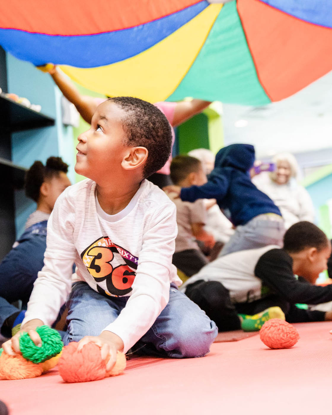 Kids playing with each other at Romp n' Roll's parachute play during mixed age classes for kids.