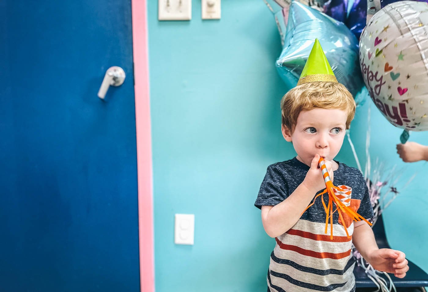 A boy with a green party hat on and birthday balloons at Romp n' Roll.