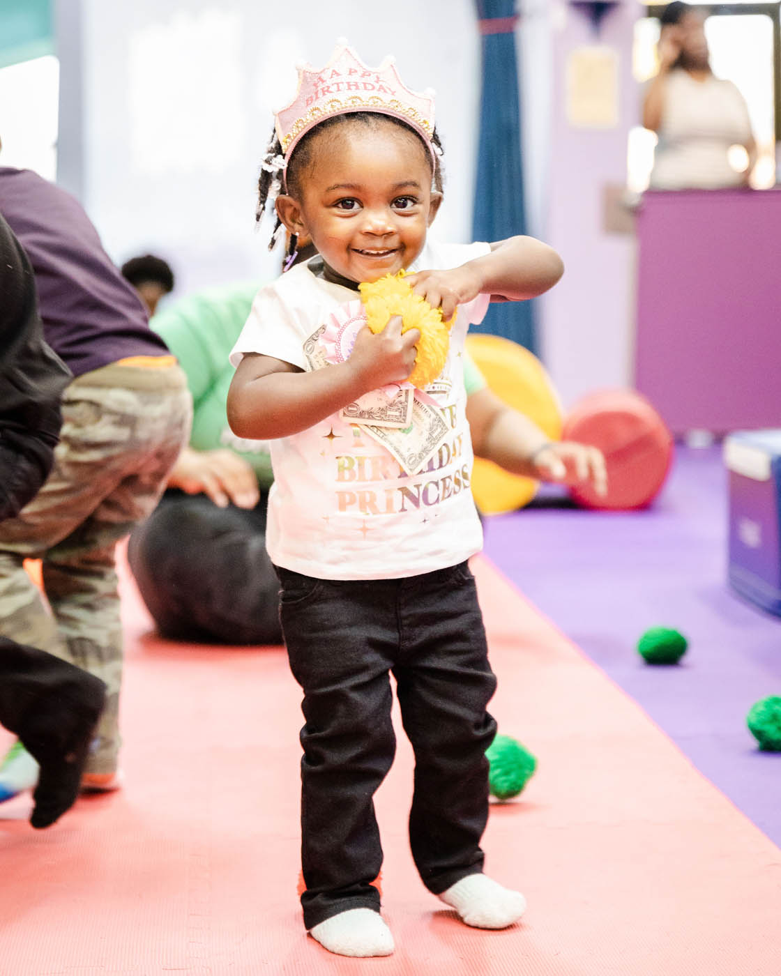 A young girl with a pink princess shirt on holding a yellow fluffy ball - Romp n' Roll children's party places in St. Petersburg, FL.