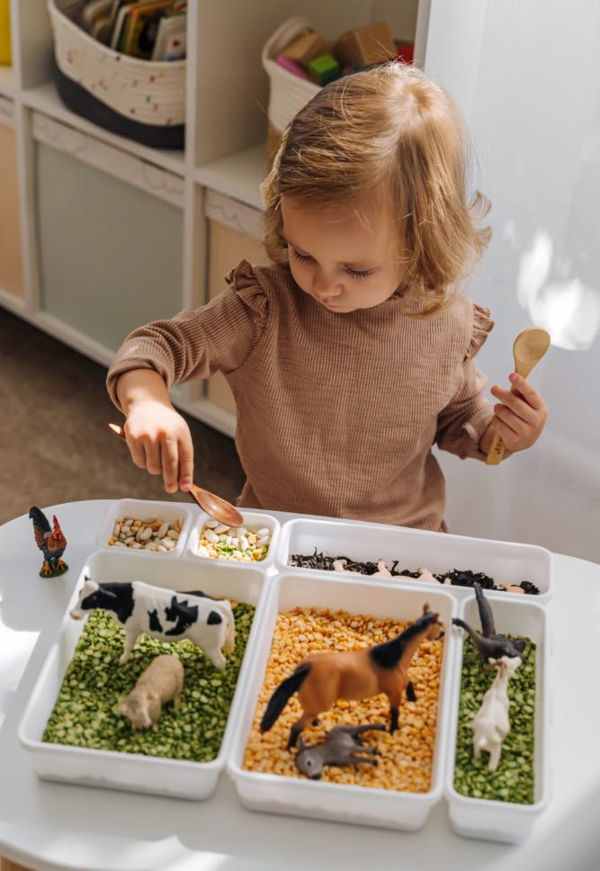 A little girl plays with a colorful sensory bin with farm animals - contact Romp n' Roll in Wethersfield, CT for sensory activities.